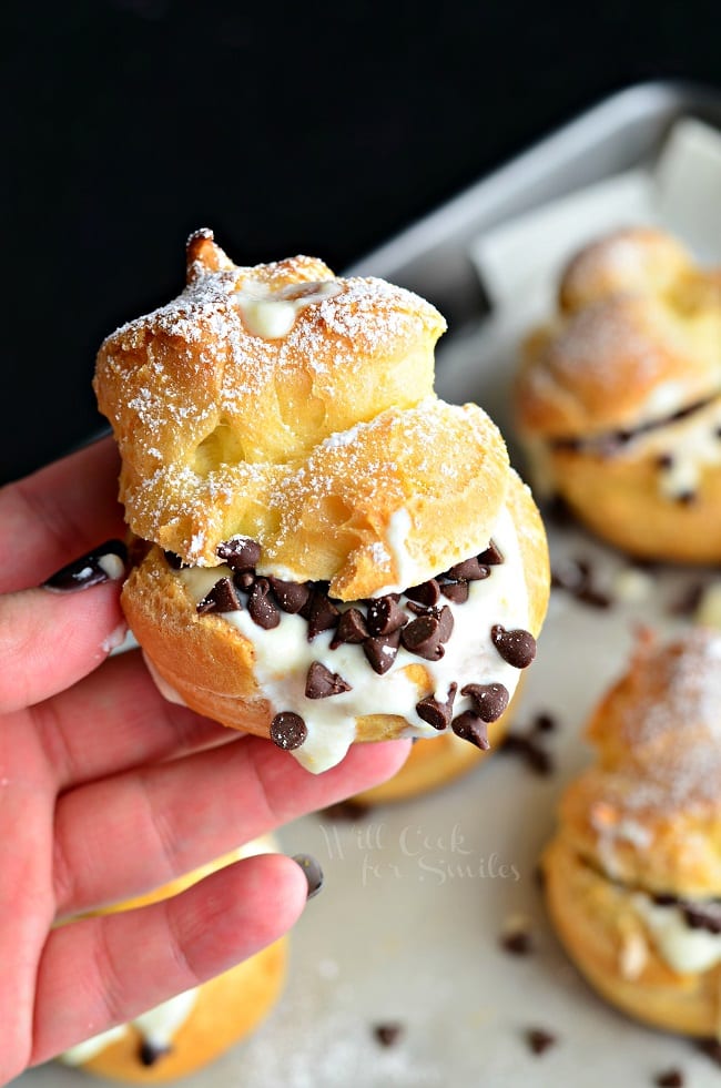holding a Cannoli Choux Pastry (Cream Puffs) with chocolate chips in the middle on a baking sheet 