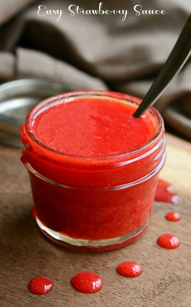 Easy Strawberry Sauce in a small mason jar with a spoon in it on a cutting board with little drops of sauce around it 