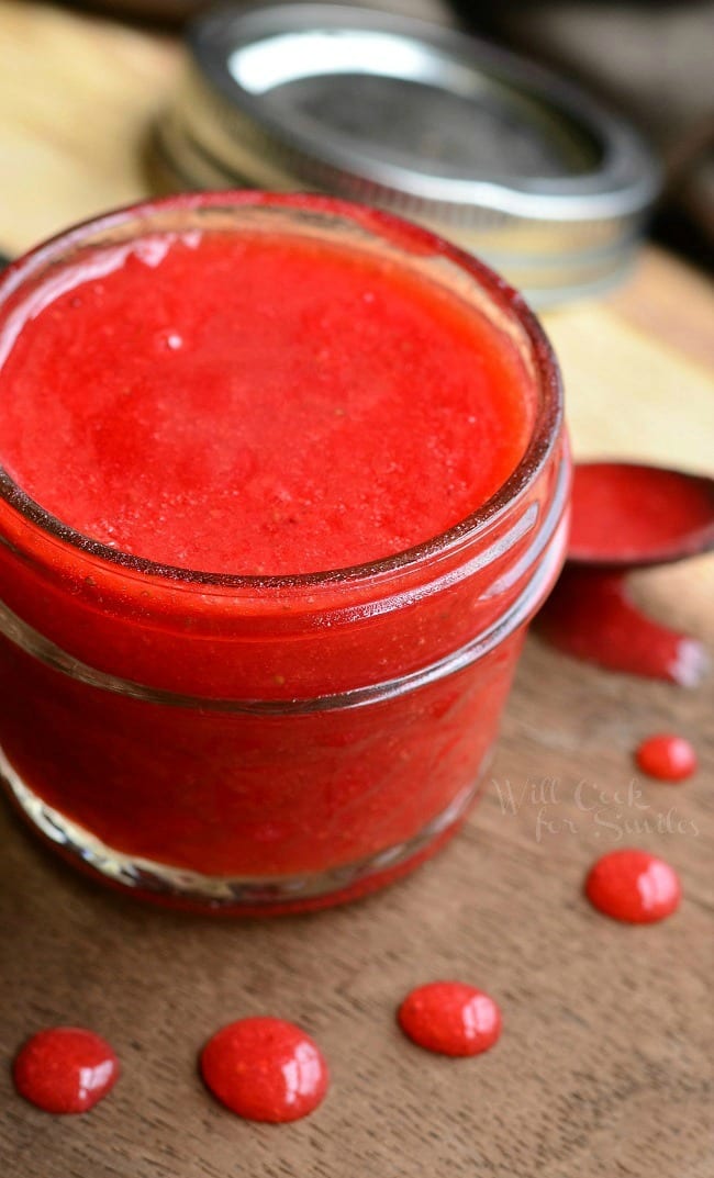 small mason jar filled with easy strawberry sauce on a wooden table and the mason lid jar in the background