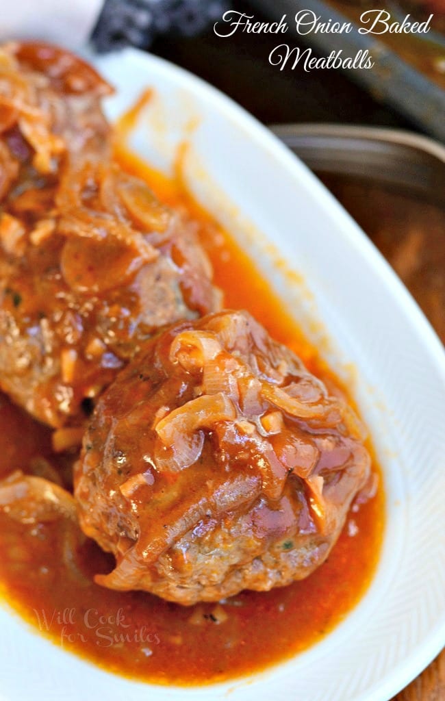 French Onion Baked Meatballs served on a white dish. Meatballs are topped with plenty of onion pieces and smothered in sauce.