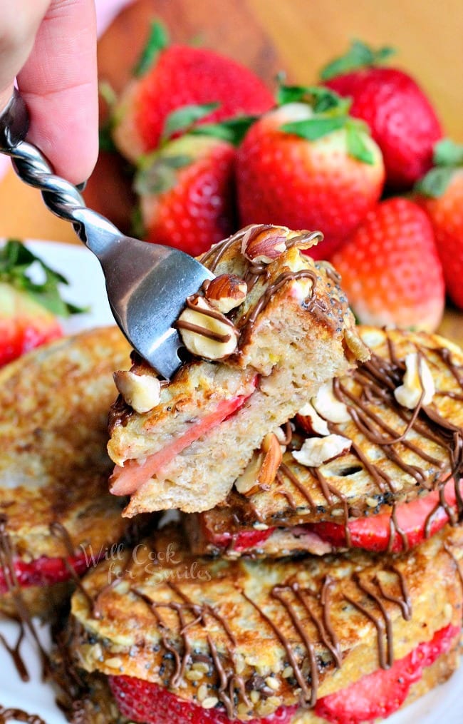 Fruit Filled Hazelnut French Toast with strawberries stacked up on a white plate with a fork lifting up a bite 