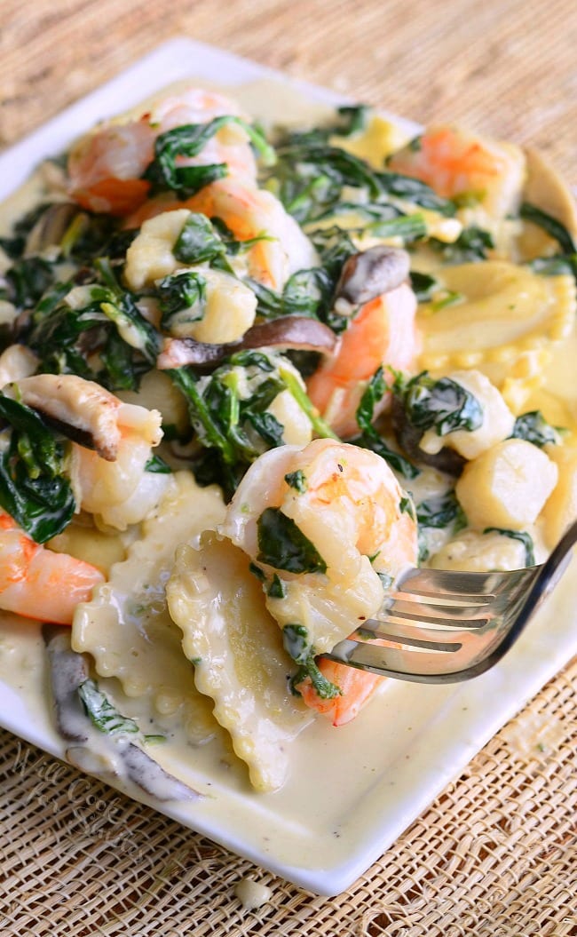 Ravioli with Seafood, Spinach & Mushrooms on a white plate with a fork lifting up a shrimp 