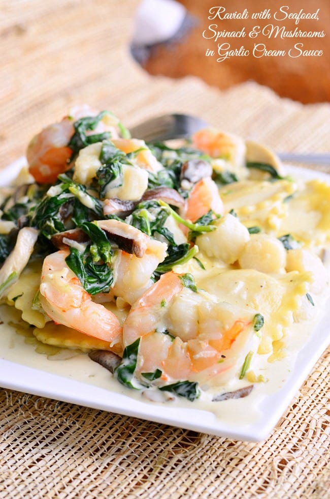 Ravioli with Seafood, Spinach & Mushrooms in Garlic Cream Sauce is presented on a small, white plate. Shrimp and spinach in this dish stand out.