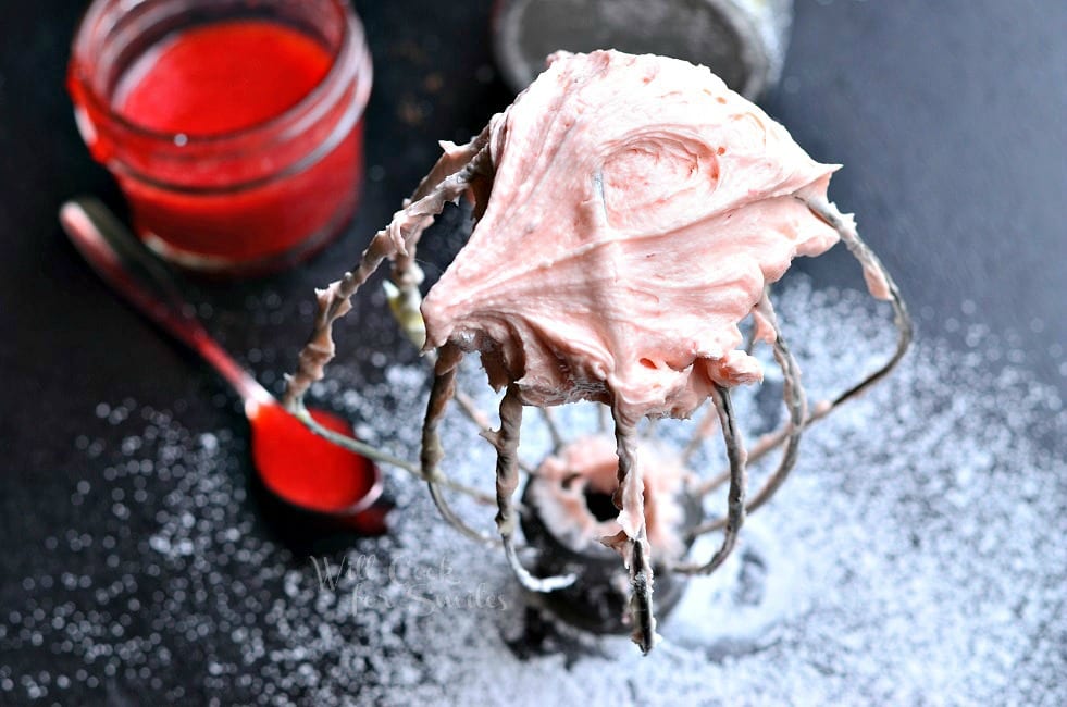 Strawberry Buttercream Frosting on a mixer whisk with strawberry sauce in a jar and on a spoon 