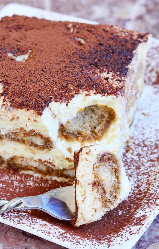 Tiramisu on a white plate with a bite on a fork 