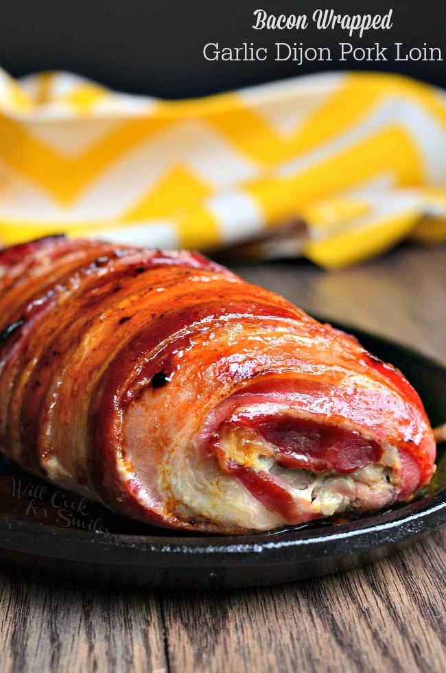 Bacon Wrapped Pork Tenderloin on a plate on a table with a yellow and white kitchen towel in the background 