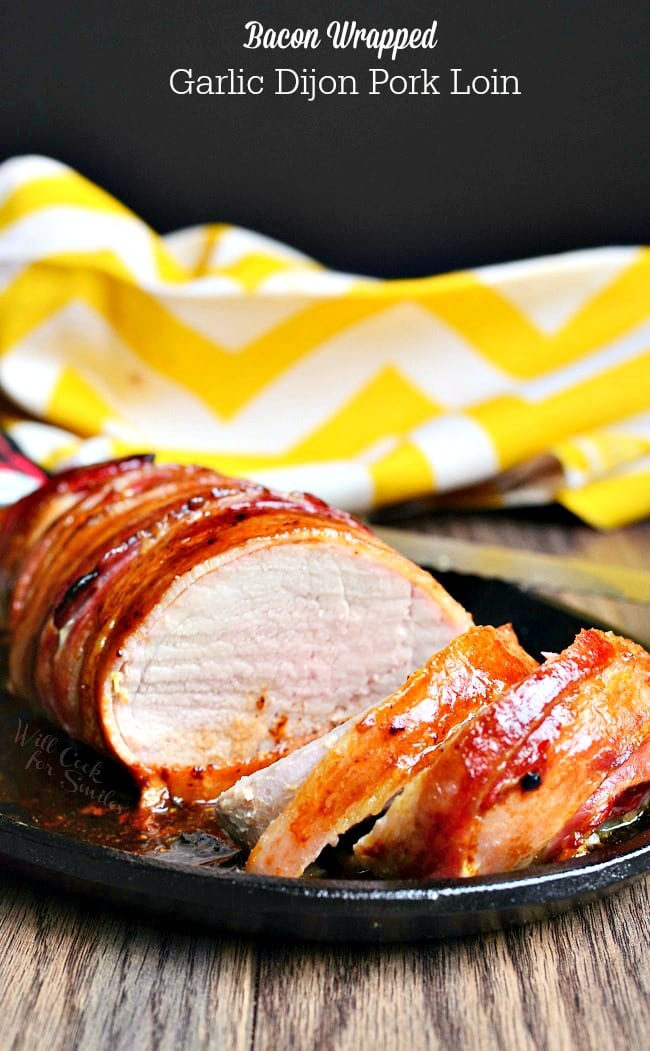 Pork Tenderloin wrapped in bacon on a black plate on a table with yellow and white towel in the background 