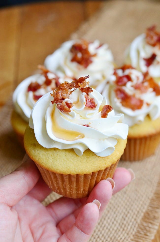holding a Maple Bacon Cupcakes with frosting and bacon crumbles and maple syrup  on top  