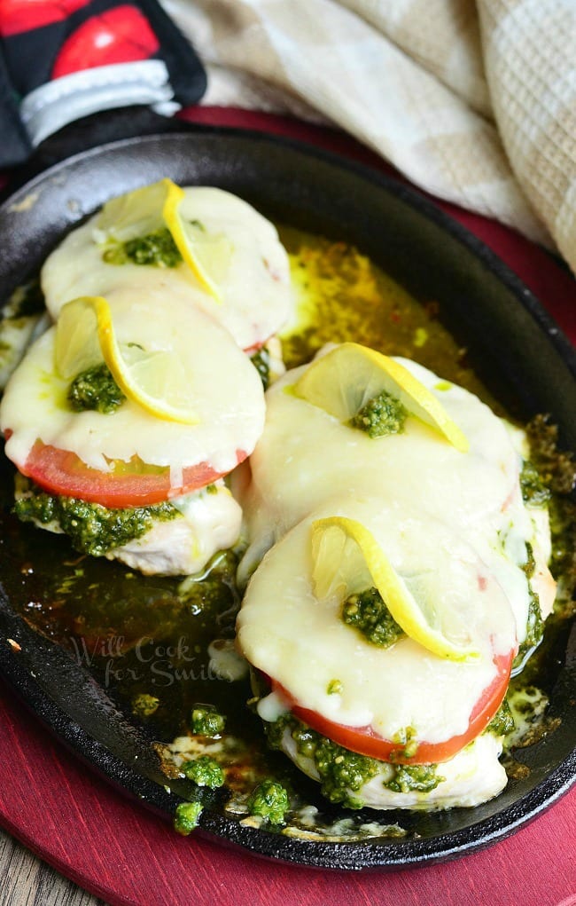 Margherita Chicken Recipe with cheese, tomato, pesto and lemon on top in a cast iron skillet 