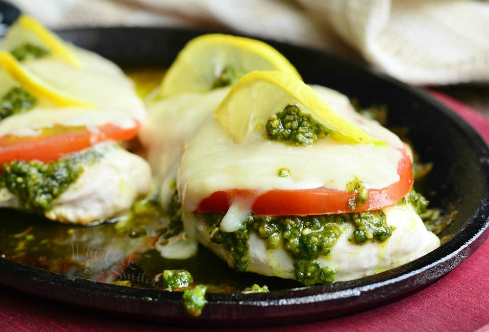 Margherita Chicken Recipe with cheese, tomato, pesto and lemon on top in a cast iron skillet 