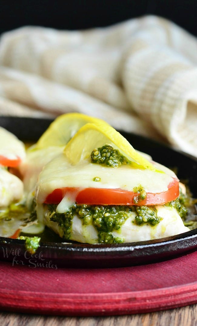 Margherita Chicken Recipe with cheese, tomato, pesto and lemon on top in a cast iron skillet 