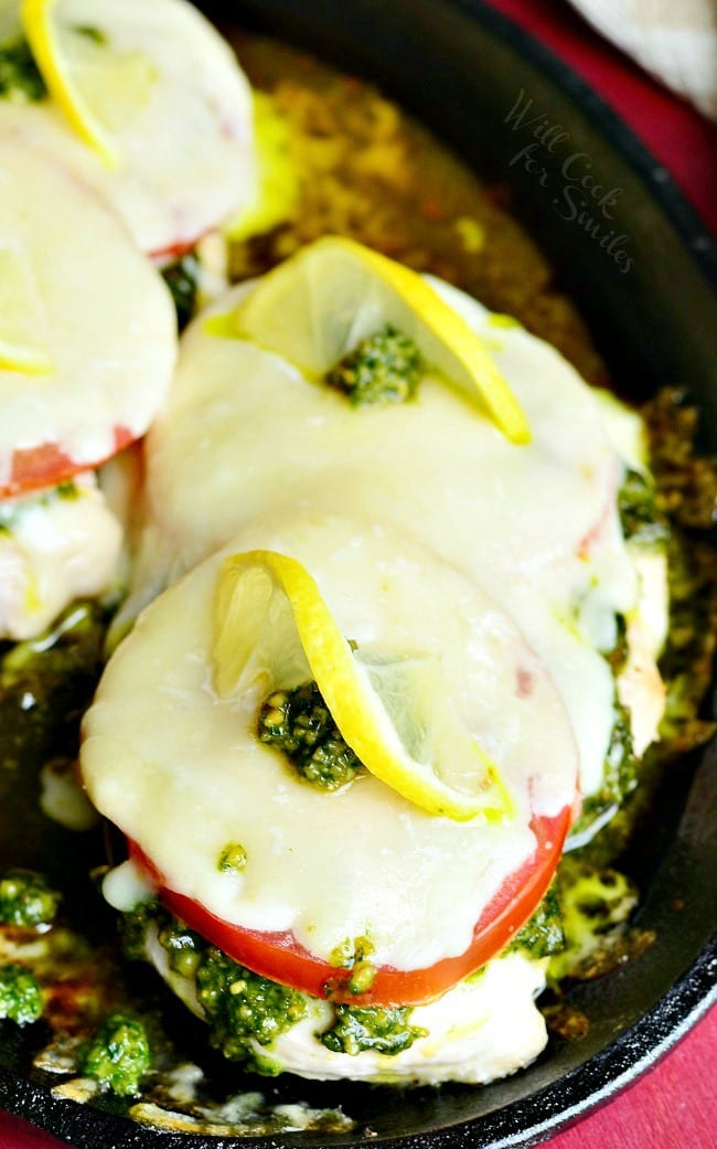 Margherita Chicken Recipe with cheese, tomato, pesto and lemon on top in a cast iron skillet 