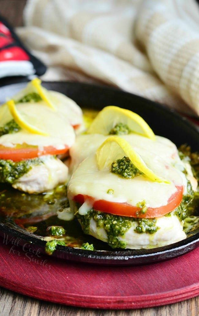 Margherita Chicken Recipe with cheese, tomato, pesto and lemon on top in a cast iron skillet 