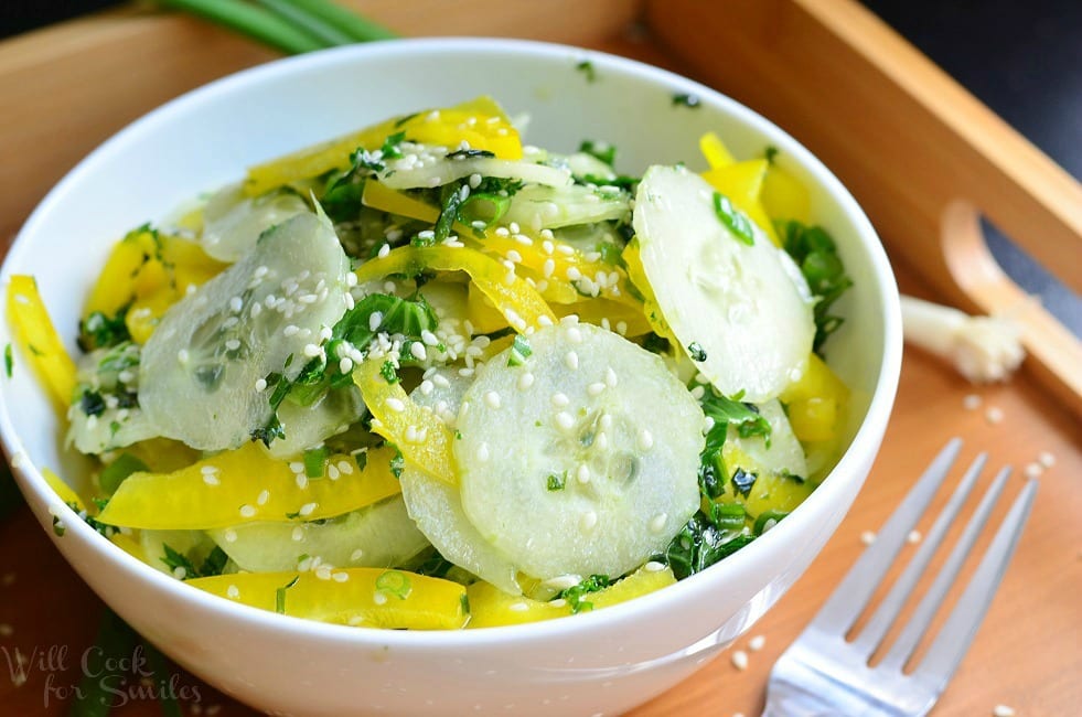 Sesame Cucumber Salad with yellow bell peppers on a wood tray with sesame seeds and a fork to the left 