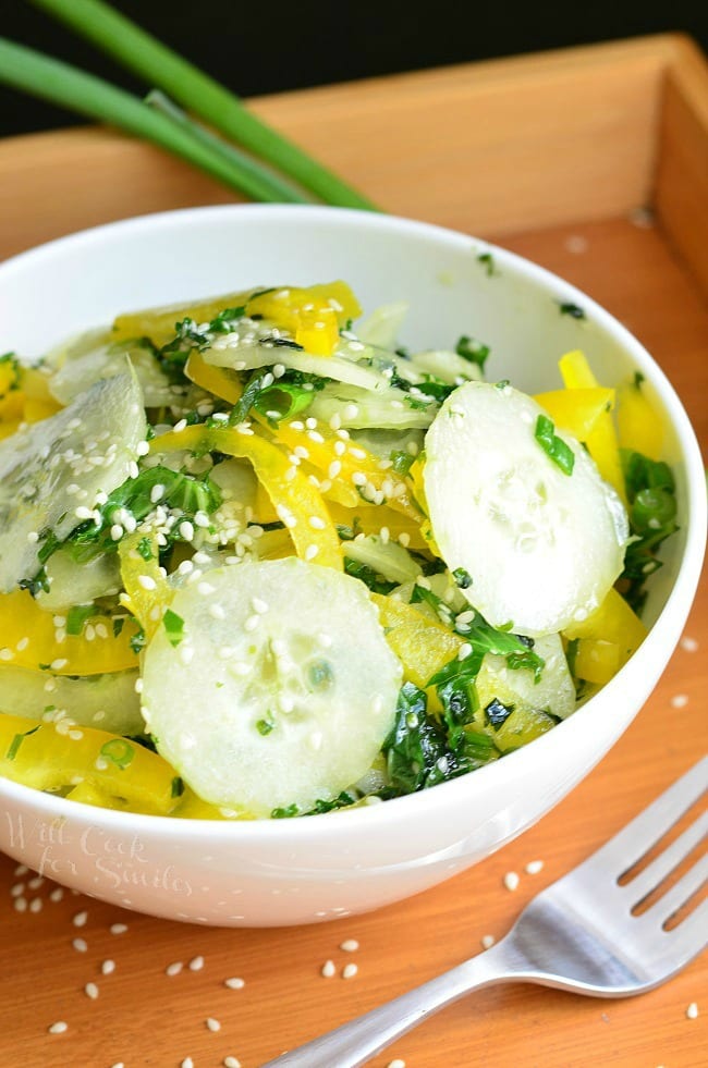 Sesame Cucumber Salad with yellow bell peppers on a wood tray with sesame seeds and a fork to the right