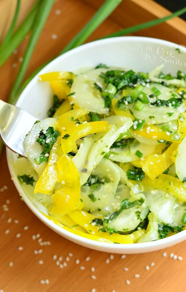 Sesame Cucumber Salad with yellow bell peppers on a wood tray with sesame seeds and a fork to the left 