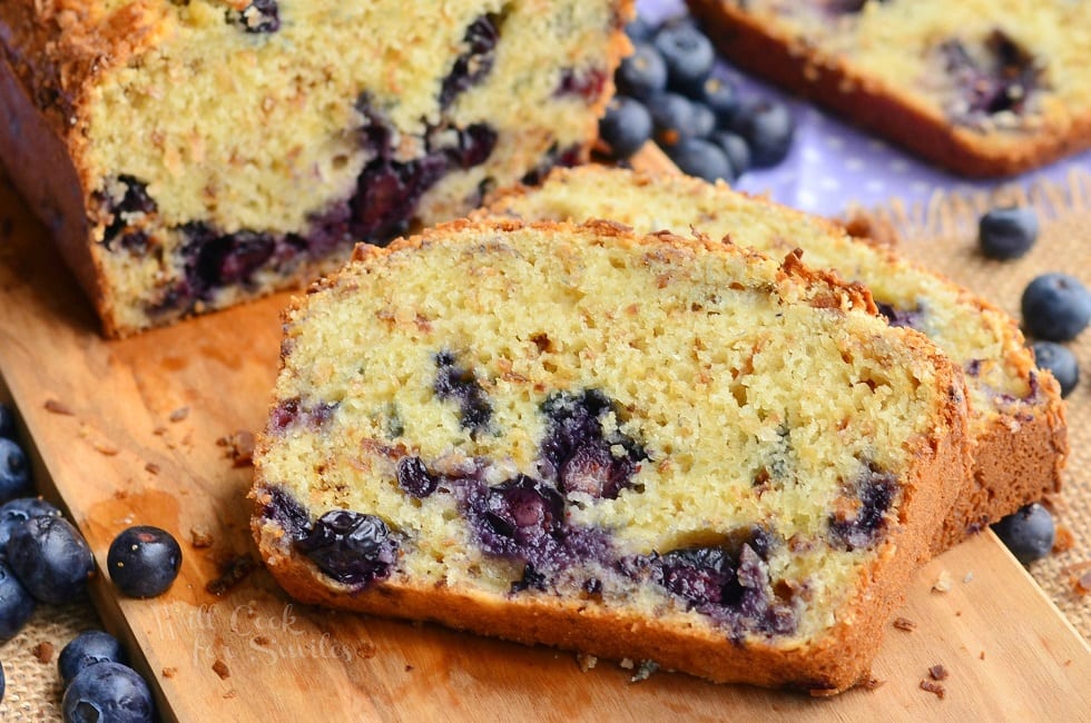 Toasted Coconut Blueberry Bread sliced on a cutting board with blueberries around it