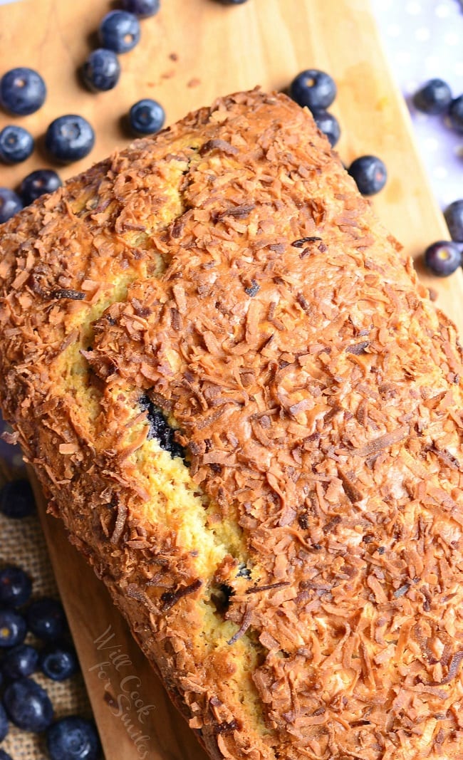 Coconut Blueberry Bread on a cutting board with blueberries around it 