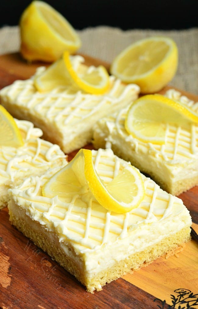 Vanilla Bean Lemon Cheesecake Bars with a lemon twist garnish on top on a wood cutting board 