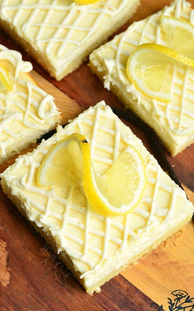 top view of Vanilla Bean Lemon Cheesecake Bars with a lemon twist garnish on top on a wood cutting board 