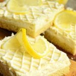 4 Vanilla bean lemon cheesecake bars on a wooden cutting board topped with sliced lemons