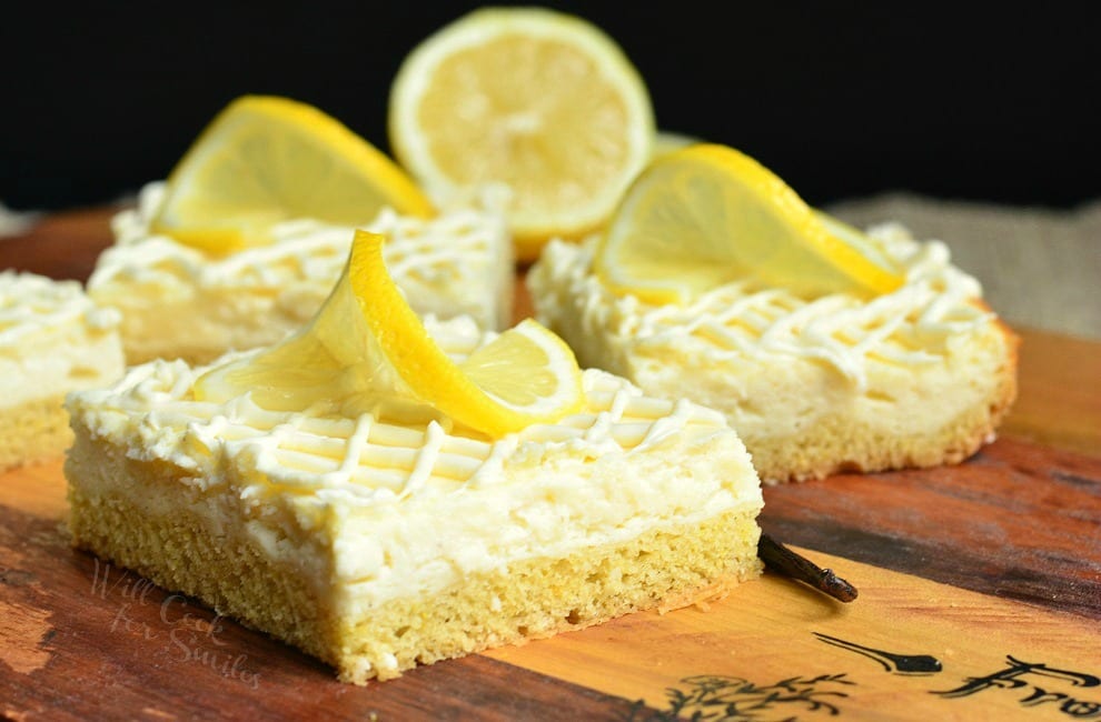 Vanilla Bean Lemon Cheesecake Bars with a lemon twist garnish on top on a wood cutting board 