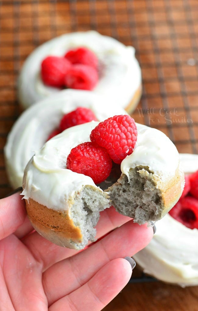 Holding a white chocolate covered baked raspberry donuts with a bite taken out of it.