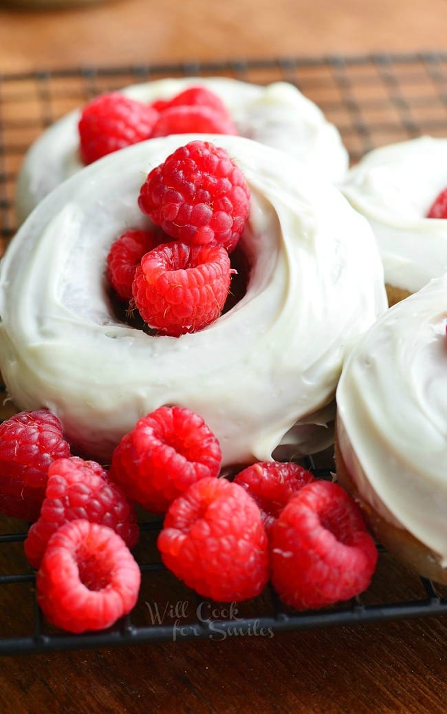 White Chocolate Covered Baked Raspberry Donuts with fresh raspberries in the middle and raspberries stacked on the front left sitting on a cooling wrack 