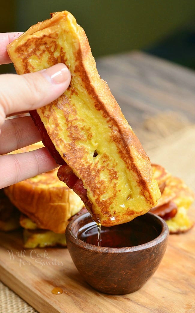 holding the french toast stick dipped in maple syrup