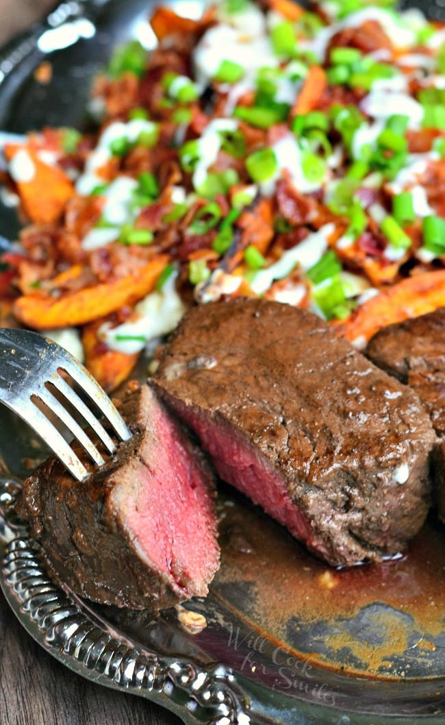 2 espresso rubbed ribeye filets on a silver platter with a side of loaded sweet potato wedges