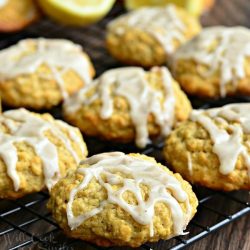 Glazed cookies on a cooling rack on a wooden table with halved lemons in between cookies