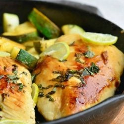 close up view of Honey key lime chicken on a black skillet on wood table with sliced zucchini behind chicken