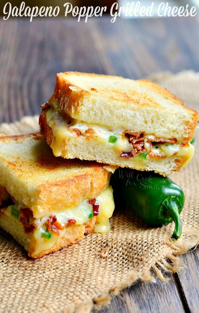 Jalapeno Popper Grilled Cheese loaded with gooey cheese, jalapenos and bacon cut in half with a jalapeno to the side 