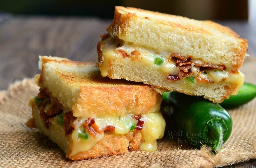 Jalapeno Popper Grilled Cheese loaded with gooey cheese, jalapenos and bacon cut in half with a jalapeno to the side 