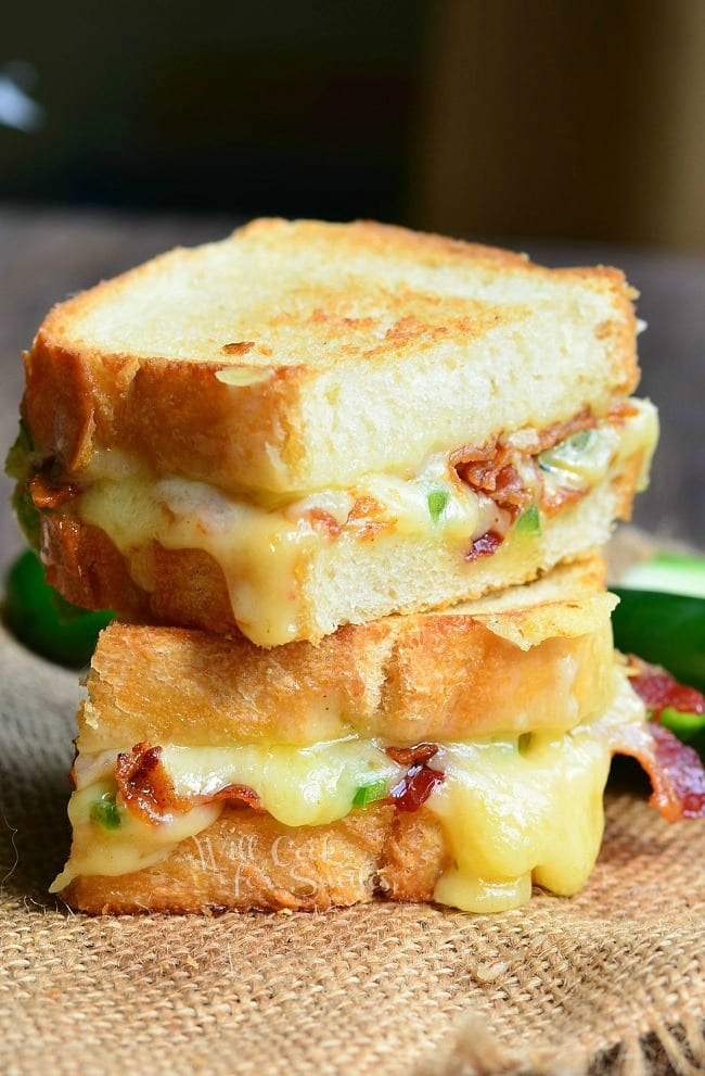 Jalapeno Popper Grilled Cheese loaded with gooey cheese, jalapenos and bacon cut in half with a jalapeno to the side 