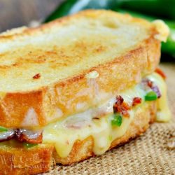 Close up view of a whole jalapeno popper grilled cheese on a burlap cloth with peppers in the background