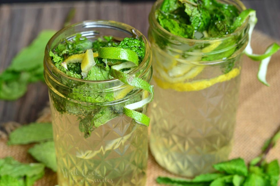 Lemon Lime Mojitos in a mason jar with limes and mint inside and around the base of the jars on the table top 