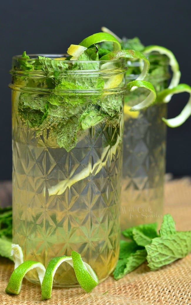 Lemon Lime Mojitos in a mason jar with limes and mint inside and around the base of the jars on the table top 