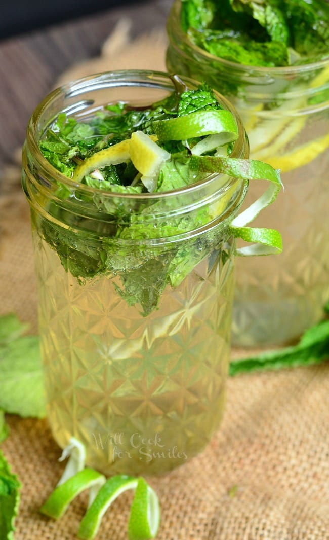 Lemon Lime Mojitos in a mason jar with limes and mint inside and around the base of the jars on the table top 