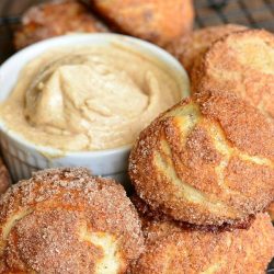 several snickerdoodle pretzel puffs on a cooling rack with dipping cream in a small white crock at center