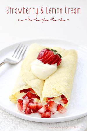 crepes with strawberries and a lemon cream inside of them with a strawberry and whipped cream on top on a white plate with a fork to the left 