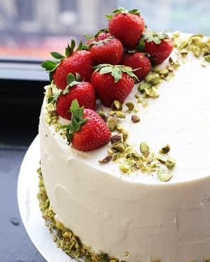 strawberry cake with white frosting and pistachios and strawberries on top  