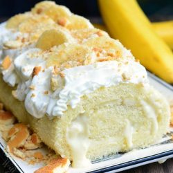 banana pudding cake roll on a decorative white rectangular plate on a wooden table with 2 bananas in the background