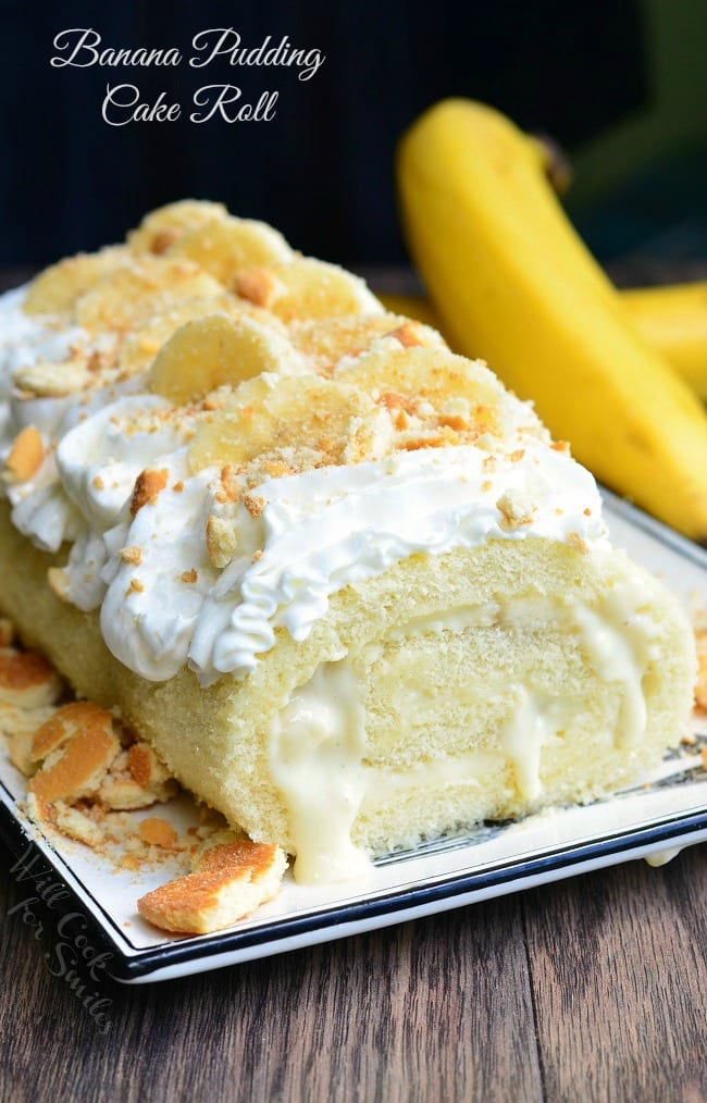 Banana Pudding Cake Roll is served on a white dish. The roll itself is oozing with filling. It's topped with whipped cream, banana slices and crumbed vanilla wafers.