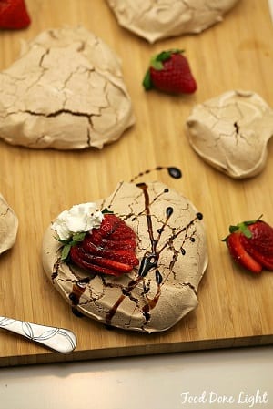 Chocolate Pavlovas with Wine Soaked Strawberries in the shape of a heart with a sliced up strawberry and whip cream on top on a cutting board 
