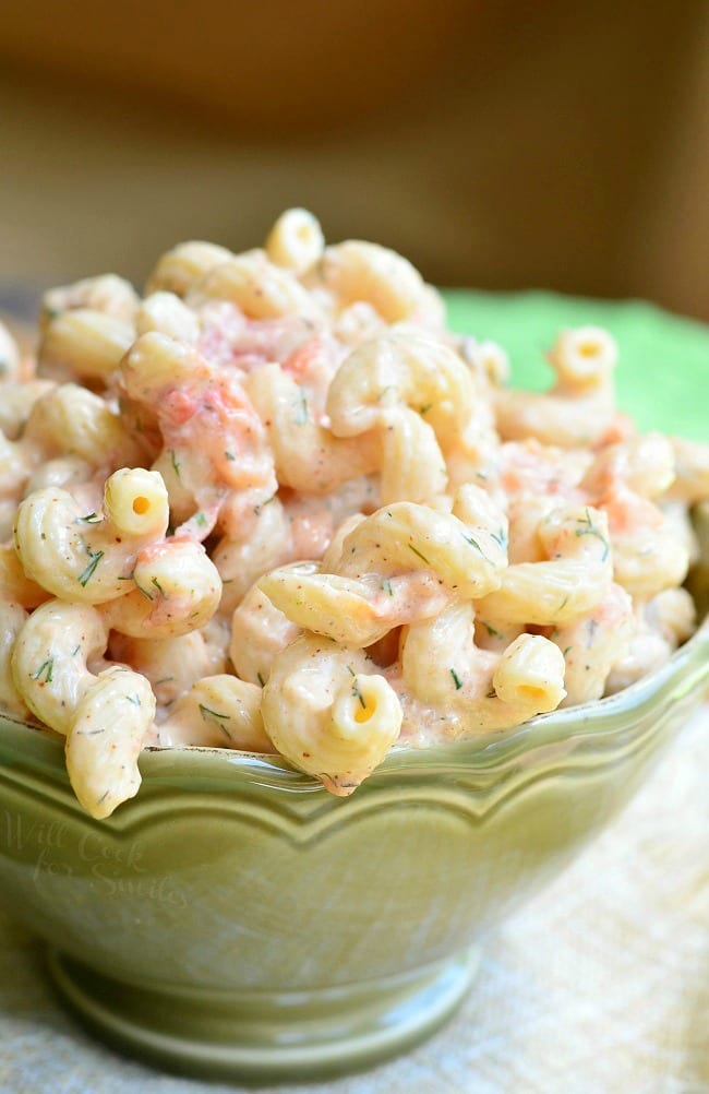 Creamy Roasted Tomato Pasta Salad is served in a green dish. There are lots of spiral noodles in a creamy sauce. Pieces of roasted tomato are seen throughout.