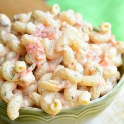 close up view of small green bowl filled with creamy roasted tomato pasta salad on a tan cloth