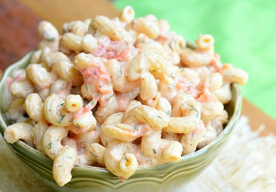 Creamy Roasted Tomato Pasta Salad is served in a green dish. There are lots of spiral noodles in a creamy coating. Pieces of roasted tomato are seen throughout.