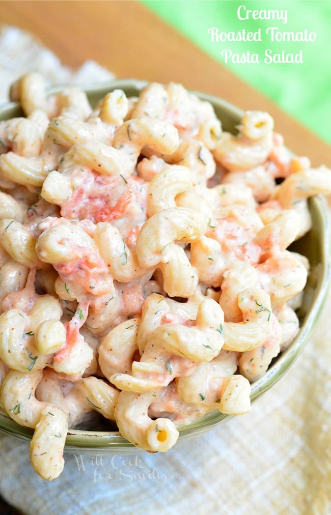 Creamy Roasted Tomato Pasta Salad is served in a green serving dish. There are lots of spiral noodles in a creamy coating. Pieces of roasted tomato are seen throughout.