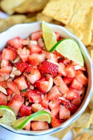 Dessert Strawberry Salsa strawberries diced up in a white bowl with lime twists on each side of the bowl 